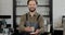 Portrait of caucasian handsome male barista and gloves giving cup of coffee to camera and smiling. Barista handing drink