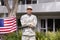 Portrait of caucasian male soldier standing in garden with american flag displayed outside house
