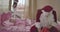 Portrait of Caucasian Santa sitting on pink bed with red gift bag while blond little girl sleeping at the background