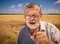 Portrait of Caucasian senior farmer singing like in karaoke while standing against wheat field at summer season