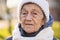 Portrait Caucasian senior woman with gray hair and deep wrinkles 90 years old posing in warm clothes, white knitted scarf and hat