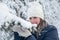 Portrait of Caucasian smiling woman touching snow cap on tree branch with her mittens, winter season