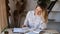 Portrait of a Caucasian teacher sitting at a wooden table with books and textbooks at home by the window. The woman is