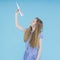Portrait of Caucasian Teenage Girl in Blue Checked Dress Launching Origami Paper Plane Posing Over Blue Background
