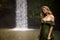 Portrait of Caucasian woman near the waterfall. Closed eyes. Enjoy nature. Water splash. Young woman wearing green dress. Travel
