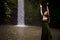 Portrait of Caucasian woman near the waterfall. Closed eyes. Hands raised up. Enjoy nature. Water splash. Woman wearing green