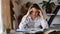 Portrait of Caucasian young tired girl sitting at a wooden table with books and textbooks at home by the window. The