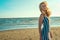 Portrait of a charming blond long-haired woman in long black and white striped dress smelling and enjoying aroma of the sea