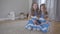 Portrait of charming brunette caucasian twin sisters switching channels with remote control. Joyful kids in blue and