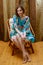 Portrait of charming girl in short silk dress at home. Bare feet on wooden floor