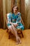 Portrait of charming girl in short silk dress at home. Bare feet on wooden floor