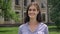 Portrait of charming happy brunette woman smiling at camera, cheerful student standing in park near college