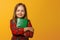 Portrait of a charming little girl in a red dress on a yellow background. Child schoolgirl holds a book. The concept of education