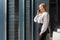 Portrait of charming positive woman smiling and talking on phone, looking out window of business center, indoors