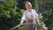 Portrait of charming senior woman watering lawn in sunshine in slow motion standing outdoors with hose. Confident