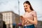 Portrait of charming woman having foxy ginger hairstyle red lips stick holding device look in city