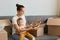 Portrait of charming young woman wearing white t shirt sitting on sofa, holding her infant baby, unpacking box with plates,