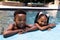 Portrait of cheerful african american siblings laughing while relaxing at poolside in resort