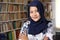 Portrait of cheerful Asian muslim female librarian wearing hijab, smiling crossed arms confidence gesture against book shell in