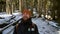 Portrait of a cheerful bearded laughing young man with a backpack standing in a coniferous winter forest