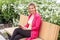 Portrait of cheerful beautiful young businesswoman in elegance style sitting in bench on park, holding tablet with toothy smile