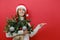 Portrait of cheerful beautiful young Santa woman wears Christmas hat hold bouquet of spruce branches point on workspace area copy