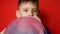 Portrait of a cheerful caucasian boy 7 years old inflating a balloon on a red background. studio shooting. The child inflates ball