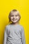 Portrait of cheerful fair-haired boy with long hair on bright yellow background. Vertical frame