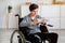 Portrait of cheerful handicapped teen boy in wheelchair using smartphone, chatting and texting in social media, indoors