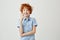 Portrait of cheerful little boy with ginger hair and freckles smiling, pointing upside with finger, having crazy