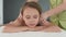 Portrait of cheerful little girl having neck, shoulder and back massage by unrecognizable female pediatric masseuse at