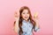 Portrait cheerful little girl with long brunette hair having fun to camera with colorful donuts isolated on pink