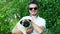 Portrait of cheerful man holds on hands cute pug dog in the park, hugs