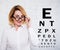 Portrait of cheerful mature business woman in eyeglasses and eyevision test chart over white wall