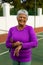 Portrait of cheerful senior woman with short hair checking time over wristwatch at tennis court