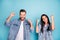 Portrait of cheerful spouses raising fists screaming yeah wearing denim jeans isolated over blue background