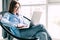 Portrait of cheerful trendy girl sitting in cane chair chatting with friends making online shopping using laptop wifi internet