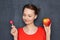 Portrait of cheerful woman holding apple and lollipop in hands