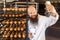 Portrait of cheerful young adult blogger baker with long beard in white uniform standing in factory and making selfie on shelves