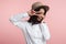 Portrait of a cheery stylish girl, shows v sign or peace gesture, wears white shirt and hat,  over pink background.