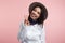 Portrait of a cheery stylish girl, shows v sign or peace gesture, wears white shirt and hat,  over pink background.