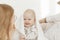 Portrait of cherubic smiling happy blue-eyed plump baby infant toddler covered with white blanket sitting on bed linen.