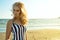 Portrait of chic blond woman in striped dress standing at the seaside and looking aside with provocative green eyes.