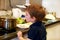 Portrait of child in kitchen. Cute little boy, playing in kitchen. Young kid is hungry, looks at and checks is it finished lunch.