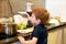 Portrait of child in kitchen. Cute little boy, playing in kitchen. Young kid is hungry, looks at and checks is it finished lunch.