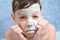 Portrait of child teen boy removing alginate mask from face looking at camera.