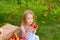 Portrait of children in an apple orchard. Little girl in blue striped dress, sits next to wicker basket with harvest of apples and