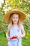 Portrait of children in apple orchard. Little girl in straw hat and blue striped dress, holding apples in hem of dress