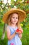 Portrait of children in an apple orchard. Little girl in straw hat and blue striped dress, holding apples in her hands