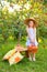 Portrait of children in an apple orchard. Little girl in straw hat and blue striped dress, holding basket with apples. Care